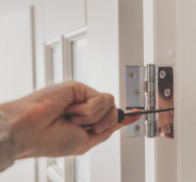 Man remove the door. Twists self-tapping screw with a screwdriver. Stainless door hinges on a white door.